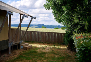 Vue du Camping Les Genêts en Occitanie, France, avec une tente, une clôture et la campagne en arrière-plan.