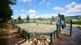Cancha multideporte en Camping Les Genêts, Occitania, Francia, con niños jugando y cielo despejado.