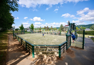 Multi-sports court at Camping Les Genêts in Occitanie, France, with children playing under blue skies.
