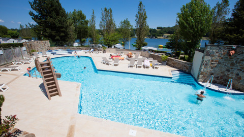 Piscina all'aperto con lettini e scivolo al Camping Les Genêts, parco vacanze in Occitania, Francia.