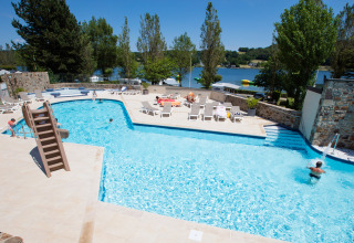 Udendørs swimmingpool med liggestole og rutsjebane på Camping Les Genêts, feriepark i Occitanie, Frankrig.