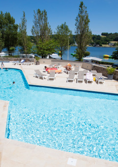 Piscina exterior con tumbonas y tobogán en Camping Les Genêts, parque vacacional en Occitania, Francia.