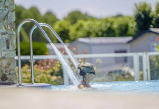 Donna che si rilassa nella piscina con getto d'acqua al Camping Les Genêts, parco vacanze in Occitania, Francia.