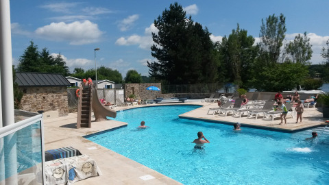 Piscina al aire libre con tobogán y tumbonas en Camping Les Genêts, parque vacacional en Occitania, Francia.