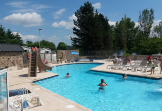 Außenpool mit Wasserrutsche und Sonnenliegen im Camping Les Genêts, Ferienpark in Okzitanien, Frankreich.