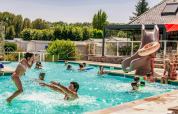 Børn og voksne leger sammen i swimmingpoolen på Camping Les Genêts feriepark i Occitanie, Frankrig.