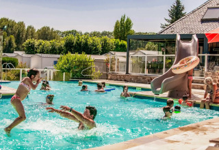 Børn og voksne leger sammen i swimmingpoolen på Camping Les Genêts feriepark i Occitanie, Frankrig.