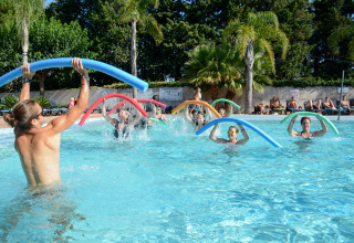 People enjoy a water aerobics class using colorful pool noodles at the outdoor pool in Camping Les Pêcheurs.
