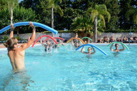 Des personnes suivent un cours d’aquagym avec des frites colorées dans la piscine extérieure du Camping Les Pêcheurs.