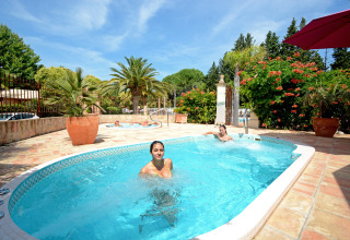 Vrouwen ontspannen in het zwembad bij Camping Les Pêcheurs, Provence-Alpes-Côte d’Azur, Frankrijk, tussen palmbomen.