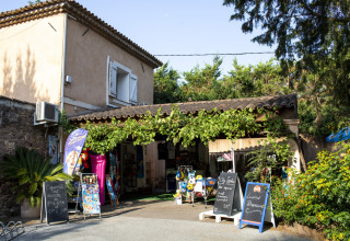 Boutique du Camping Les Pêcheurs en Provence-Alpes-Côte d’Azur, France, entourée de verdure et de panneaux.