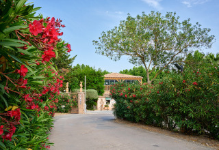 Toegang tot Camping Les Pêcheurs in Provence-Alpes-Côte d’Azur, omgeven door weelderig groen en rode bloemen.