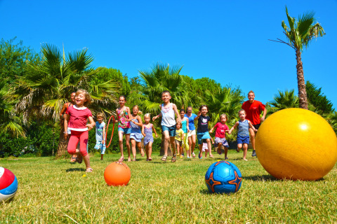 Niños juegan con pelotas en el césped bajo el sol en Camping Les Pêcheurs en Provence-Alpes-Côte d’Azur, Francia.