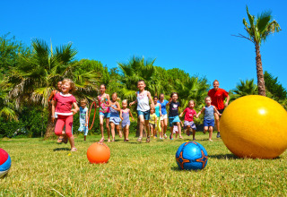 Des enfants jouent avec des ballons sur la pelouse au soleil au Camping Les Pêcheurs en Provence-Alpes-Côte d’Azur, France.