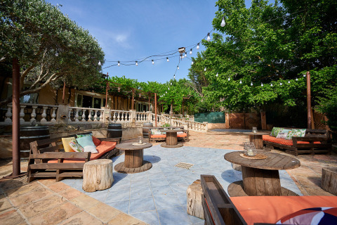 Outdoor lounge area with string lights, wooden seating, tables and lush greenery at Camping Les Pêcheurs.