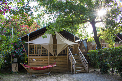 Tienda de glamping en Camping Les Pêcheurs, Provenza-Alpes-Costa Azul, Francia, con hamaca y luz solar.