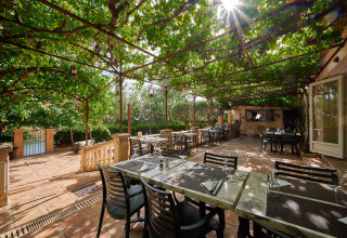 Zona pranzo all'aperto al Camping Les Pêcheurs in Provenza con pergolato verde e tavoli apparecchiati al sole.