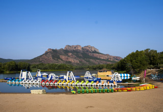 View of an inflatable water park and rowboats on the lake with mountains behind at Camping Les Pêcheurs, France.