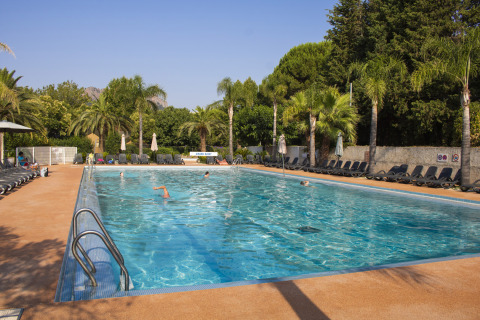 Piscina all'aperto circondata da lettini e palme al Camping Les Pêcheurs in Provenza-Alpi-Costa Azzurra, Francia.