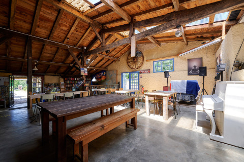 Interno di una sala comune con travi in legno, tavoli e pianoforte bianco a Camping Lestaubière, Francia.