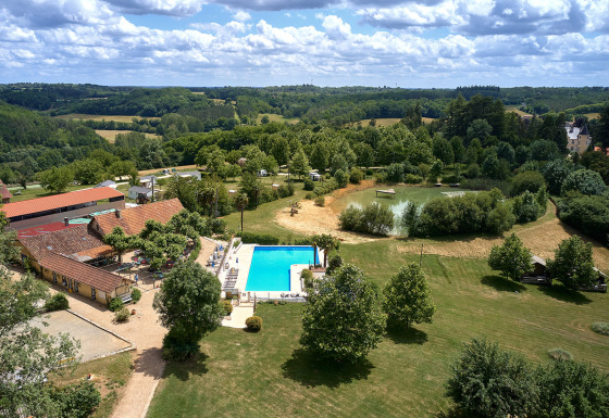 Luftfoto af Camping Lestaubière i Nouvelle-Aquitaine, Frankrig, med swimmingpool, sø og grønne marker.
