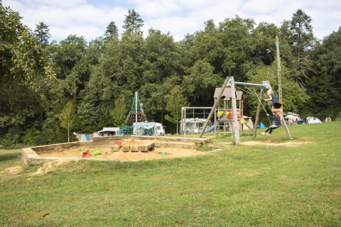Bambini che giocano nel parco giochi a Camping Lestaubière, tra alberi e camper in Nouvelle-Aquitaine.