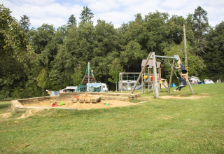 Bambini che giocano nel parco giochi a Camping Lestaubière, tra alberi e camper in Nouvelle-Aquitaine.