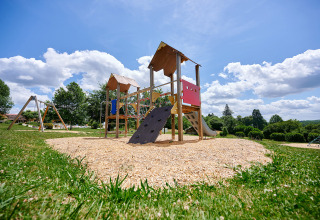 Parque infantil con estructura para escalar y tobogán en Camping Lestaubière, rodeado de naturaleza verde.