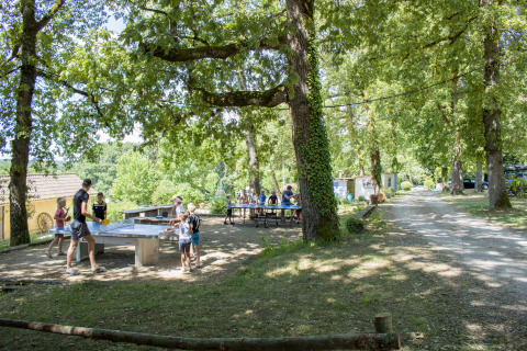 Børn og voksne spiller bordtennis i skyggen af træer på Camping Lestaubière i Nouvelle-Aquitaine, Frankrig.