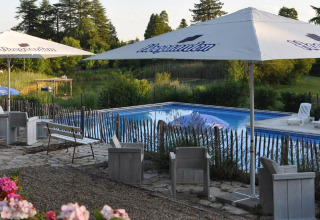 Area salotto con ombrelloni vicino alla piscina di Camping Lestaubière, villaggio vacanze in Nouvelle-Aquitaine, Francia.