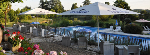 Zithoek met parasols bij het zwembad aan Camping Lestaubière, een vakantiepark in Nouvelle-Aquitaine, Frankrijk.