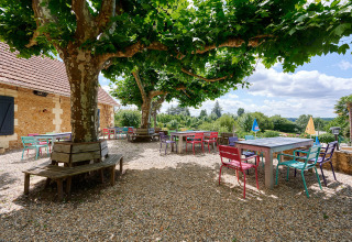 Colorful outdoor tables and chairs under leafy trees at Camping Lestaubière holiday park in Nouvelle-Aquitaine, France.