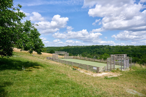 Outdoor-Sportplatz mit Holzzäunen auf einer Wiese und Blick ins Grüne bei Camping Lestaubière, Frankreich.