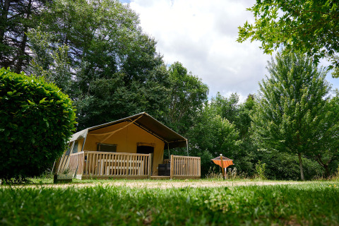 Een gezellige safaritent met houten terras in het groen op Camping Lestaubière, Nouvelle-Aquitaine, Frankrijk.