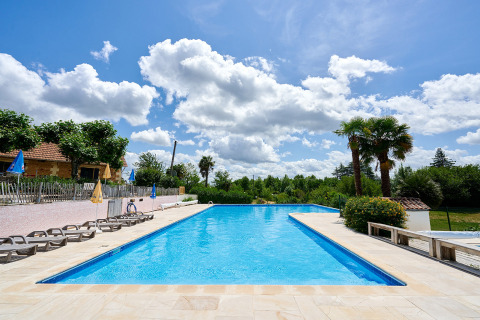 Piscine extérieure du Camping Lestaubière avec transats et palmiers sous un ciel bleu en Nouvelle-Aquitaine.