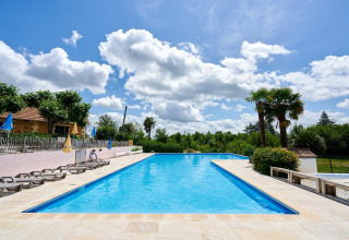 Outdoor swimming pool at Camping Lestaubière holiday park with sun loungers and palm trees in Nouvelle-Aquitaine.