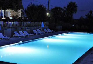 Oplyst swimmingpool ved Camping Lestaubière i Nouvelle-Aquitaine, Frankrig, med liggestole og terrasse om aftenen.