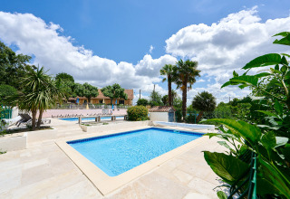 Udendørs swimmingpool i ferieparken Camping Lestaubière i Nouvelle-Aquitaine, Frankrig, under en blå himmel.