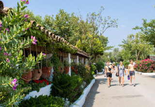 Ospiti passeggiano al sole al Camping Nautic Almata, Catalogna, Spagna, circondati da piante e fiori colorati.