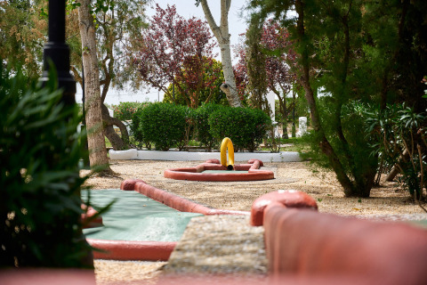 Una buca di minigolf circondata da alberi verdi al Camping Nautic Almata, parco vacanze in Catalogna, Spagna.
