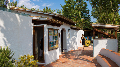 Eine Frau geht an einem weißen Gebäude mit Terrakottafliesen im Camping Nautic Almata in Katalonien, Spanien vorbei.