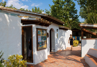 Eine Frau geht an einem weißen Gebäude mit Terrakottafliesen im Camping Nautic Almata in Katalonien, Spanien vorbei.