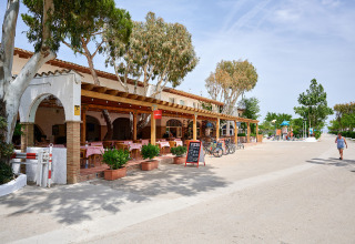 Udendørs restaurant med røde duge og cykler parkeret foran på Camping Nautic Almata i Catalonien, Spanien.