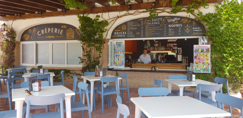 Cafetería al aire libre con sillas azules y menús en Camping Nautic Almata, Cataluña, España, de día.