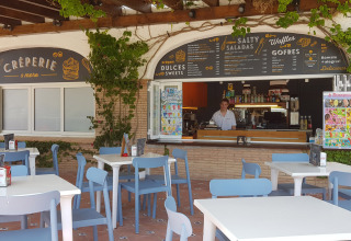 Caffetteria all'aperto con sedie blu e menù al Camping Nautic Almata, Catalogna, Spagna, durante il giorno.