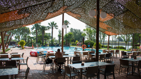 Area salotto all'aperto all'ombra con tavoli e sedie accanto alla piscina al Camping Nautic Almata in Catalogna.