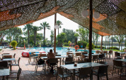 Area salotto all'aperto all'ombra con tavoli e sedie accanto alla piscina al Camping Nautic Almata in Catalogna.