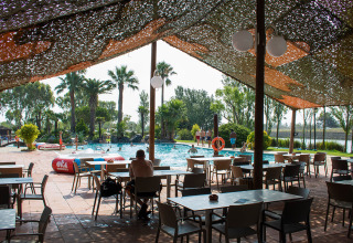 Shaded outdoor seating area with tables and chairs by the pool at Camping Nautic Almata holiday park in Catalonia.