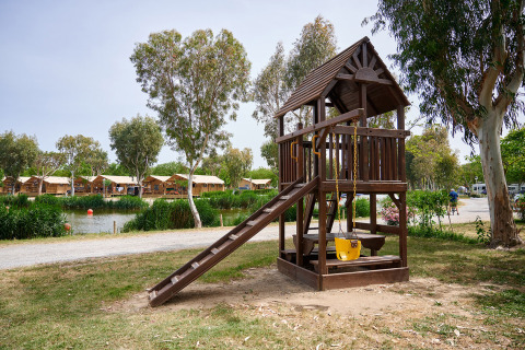 Area giochi in legno con scivolo e altalena al Camping Nautic Almata, un villaggio vacanze in Catalogna.