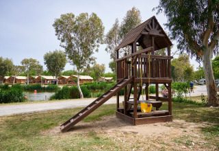 Legeplads med trægyngesæt ved sø og træer på Camping Nautic Almata feriepark i Catalonien, Spanien.